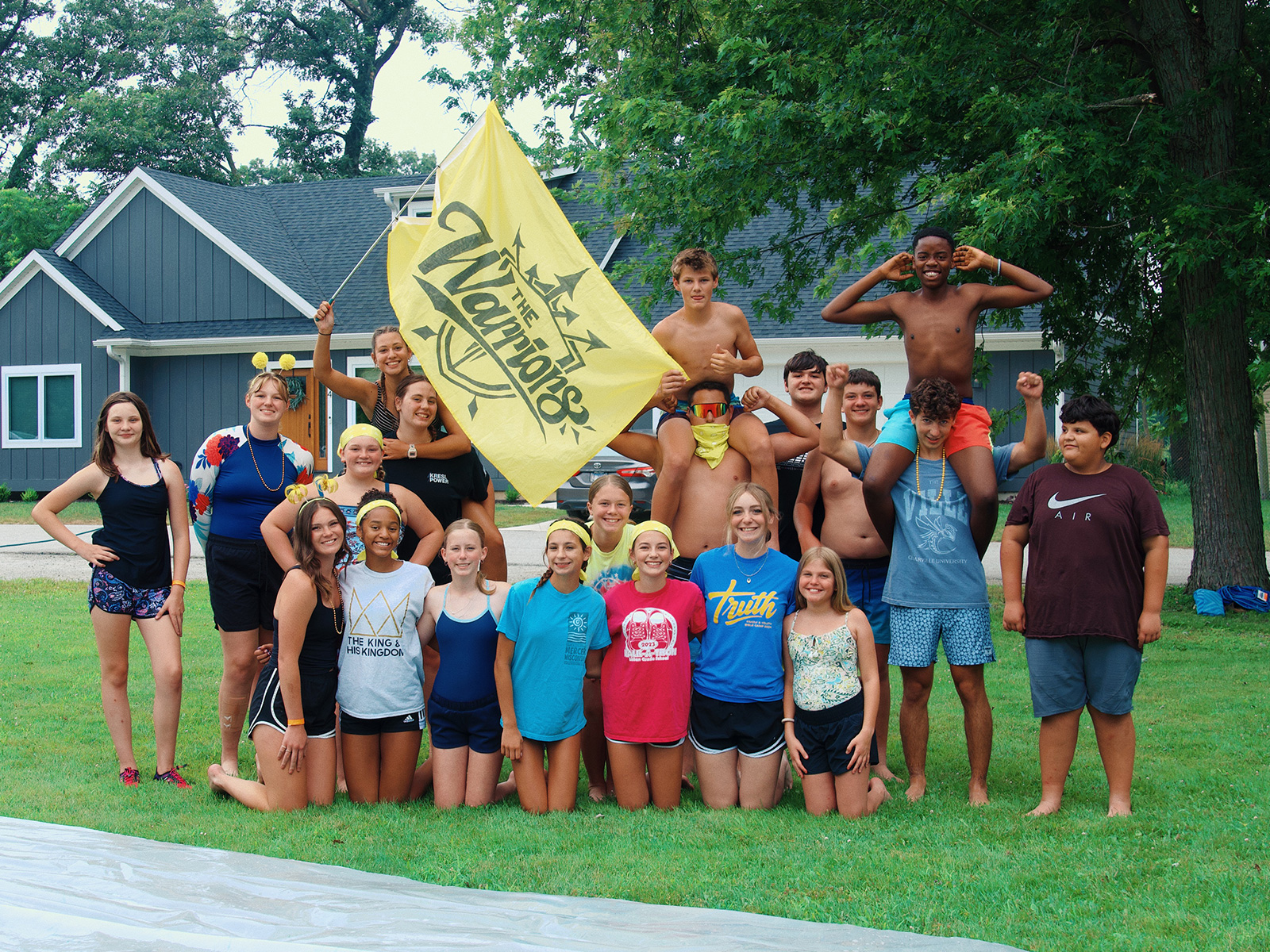 Students posing together outdoors with a yellow flag at camp